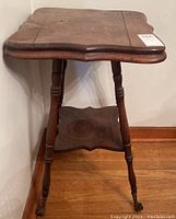 Front view of square wood side table showing beveled edges, turned legs, bottom shelf, and casters, with visible crack and water marks on top.