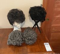 View of four wigs displayed on two wig stands and flat, showing different textures and colors.