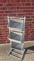 Full view of the 3 tier basket stand leaning against a brick wall outside.