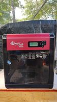 Front view of printer showing red and black housing, branding, LCD display, control buttons and feature icons.