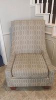 Front view of beige geometric pattern accent chair showing cushioned seat and nailhead trim