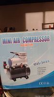 Box front showing mini air compressor image and features (oil-less, powerful, compact, reliable, quiet).