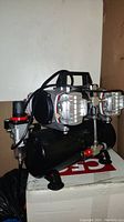 Side view of black air compressor showing dual silver pistons, pressure regulator, and part of carry handle.