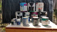 Front view of multiple paint cans arranged on a table, showing different sizes and brands including Behr and Valspar.