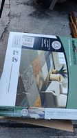 Photo showing a box of TrafficMASTER self-stick assorted carpet tile with image of assorted patterned tiles on front and measurement details