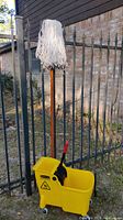 Yellow mop bucket with wood handled mop attached, outdoor setting
