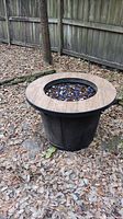 Full view of the outdoor fire pit placed on ground covered with dry leaves and grass.
