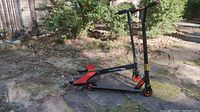 Side view photo showing the black Mongoose scooter with orange wheels and orange footplate detail on a stone paving.