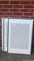 Two silver metal picture frames shown leaning against brick wall, displaying overall size and condition