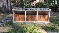 Front view of the white storage bench with cushion and three wicker baskets inside cubbies.