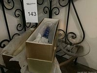 Photo showing one glass candle stick partially in original box with tissue paper and a second glass candle stick placed out of the box on a flat surface, all placed near an iron decorative background.