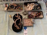 Assorted jewelry spread showing multiple pieces including beaded necklace, bracelets, earrings, and brooches on a light blue cloth.