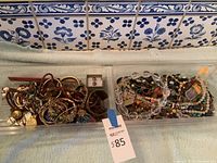 Two plastic trays containing assorted bracelets, necklaces, and loose beads