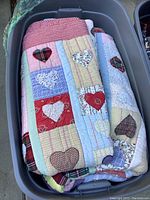 Plastic bin containing folded handmade quilts with patchwork heart designs