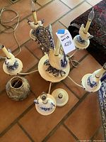 Chandelier disassembled on tiled floor showing central rooster figurine, four arms with chicken-figure candle sockets, and one removed porcelain shade.