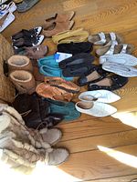 Overview photo showing a variety of women's footwear on wood floor including boots, loafers, sandals, and flats in various colors and materials.