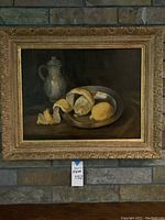 Full view of framed painting showing still life of lemons and pitcher against stone background