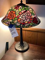 Full view of the lamp showing stained glass shade and metal base, lamp turned on.