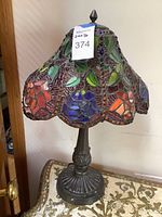 Full view of lamp showing stained glass shade with floral and leaf pattern in multiple colors and dark metal base