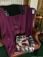 Leather wingback chair seen with maroon crocheted blanket and patchwork quilt featuring cardinals and trees