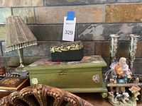 Photo showing two pewter candle sticks with grapevine design, small metallic lamp with fringed shade, green wooden music box with floral painting, and jewelry containers including small decorative box