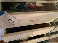 Three white drawers partially opened showing assorted purses, gloves, and cloth items inside.