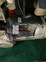 Stack of men's shirts in plastic packaging, varying colors including dark gray, purple, beige
