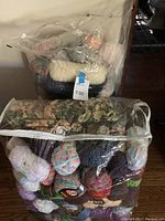 Two large clear plastic bags filled with various yarn skeins and balls in multiple colors and types.