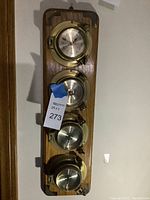 Full view of four brass maritime instruments mounted on wooden backboard, showing clock, barometer, thermometer, and hygrometer with aged brass and glass faces.