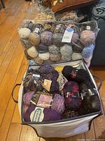 Three bags filled with many skeins and balls of yarn of various types, colors, and brands placed on wooden floor.