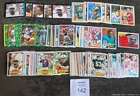 Full view of a large spread of 226 Topps Football Cards from the 1980-1988 era arranged on a dark surface, displaying various player cards with distinct designs and colors.