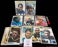Photo showing a selection of oversized 1980 Topps Super Football cards arranged with a Sharpie pen for scale. Players shown include Walter Payton, Franco Harris, Terry Bradshaw, Joe Theismann, and others.