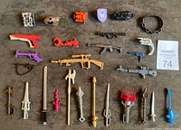 Top-down view of the 29 assorted 1980s toy weapons and accessories arranged on a grey cloth surface.