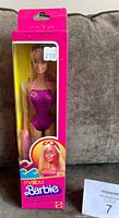 Front view of unopened Malibu Barbie doll in original pink box with clear display window, purple swimsuit and beach towel visible.