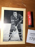 Full view of the black and white Beehive hockey photo of Bernard Geoffrion in uniform holding a hockey stick, signed in blue ink.