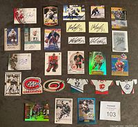 Overview of 25 autographed NHL trading cards and memorabilia arranged on a dark surface showing variety of players and teams.