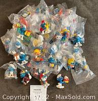 Top view of 56 Smurfs figurines mostly in clear plastic bags arranged on a surface showing a large variety of characters and colors.