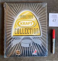 Front view of sealed 1998/1999 Kraft Collection hockey card factory set binder with bold gold and white logo on black background.