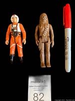 Front view of Chewbacca and Luke Skywalker figures with a Sharpie pen for size reference and MaxSold auction paper.