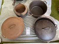 Four cast iron pots including two with lids and one smaller kettle, showing overall rust and wear.