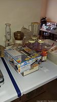 Overview of the lot showing the boxed Cookie Pro cookie press, blender, small glass jars, and hand blender or food processor base on a white table.