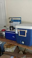 Various coolers stacked on wooden shelf along with a camping lantern and metal container