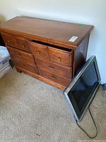 Six drawer wooden dresser with visible scratches and metal handles in medium brown finish, placed beside a JVC TV on carpeted floor.