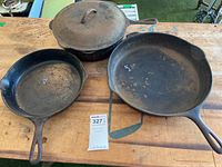 Three cast iron skillets displayed on wooden surface, one with matching lid. All show rust and wear.