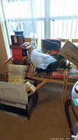 Photo showing stacked decorative boxes, wrapped artificial tree, and plastic bins on chairs and floor near window