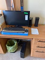 Overview of Samsung 24-inch monitor, wired keyboard, wired mouse and black desktop speakers placed on a wooden desk. HP Pavilion desktop computer tower under desk to the right.