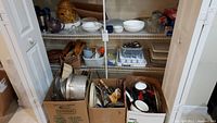 Boxes and shelves filled with assorted kitchenware items including baking dishes, bowls, pots, pans, utensils and trays.