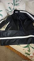 Full view of black motorcycle racing leather jacket and pants laid out on a floral couch showing white stripes on sleeves and legs.