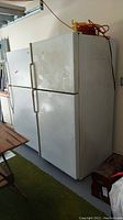 Side and front view of the white top-freezer refrigerator, showing rust spots on doors and sides, scratches on surface.