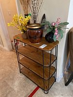 Front and top view of wood and metal shelf with assorted vases and decor including a brown and gold vase, black vase with pink orchid, yellow faux flowers in wicker basket, and pussy willow branches.